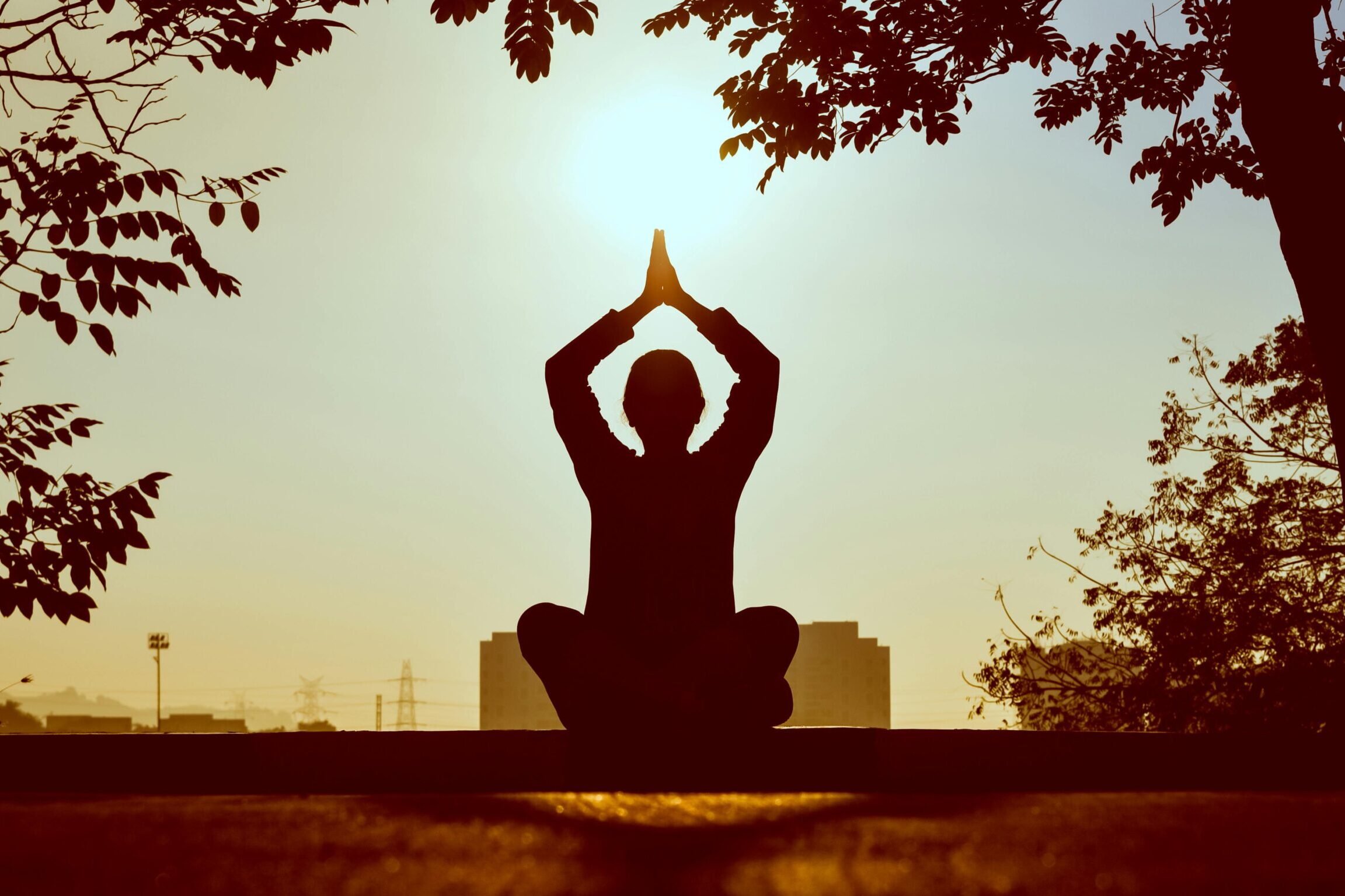 Silhouette of a person practicing yoga outdoors during sunrise, creating a calming atmosphere.